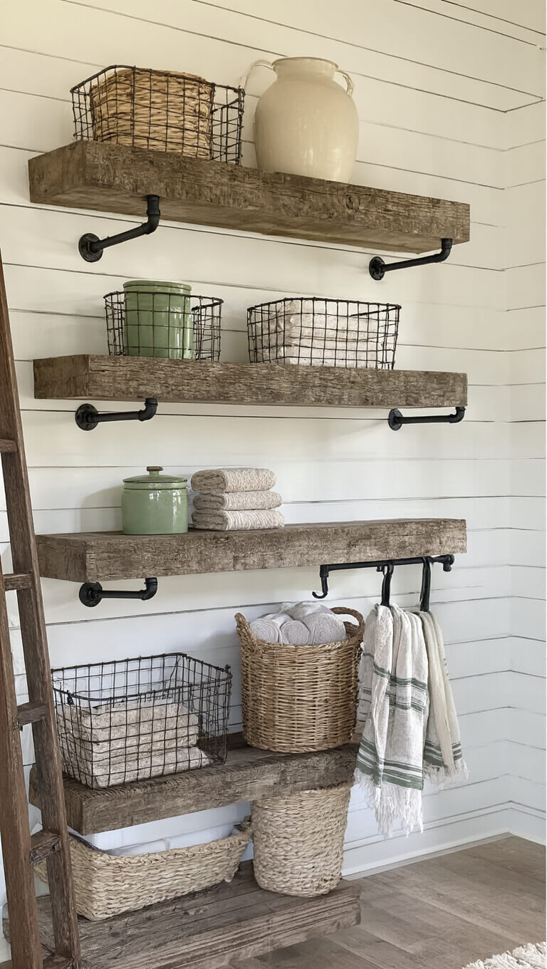 Reclaimed barn wood shelving on white shiplap wall with vintage baskets, earthenware, and rolled sage and cream towels in golden hour light.